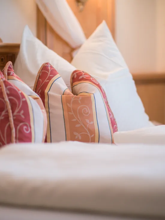 Gemütliches Hotelbett mit weißer Bettwäsche und dekorativen roten und orangefarbenen Kissen